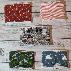 Könnte beinhalten: Fünf Fleece-Nackenwärmer mit verschiedenen Mustern. Designs umfassen Rot mit Schneemannfiguren, rot-weiße Streifen, einen grauen Eulen-Print, grüne Dinosaurier und einen blauen Eisbären-Print. Jeder Wärmer hat ein weißes, flauschiges Futter.
