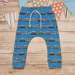 Può includere: Pantaloni blu per neonato con un motivo di furgoni colorati. I pantaloni hanno un cordoncino bianco.