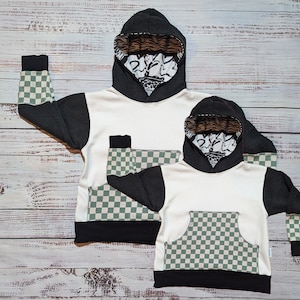 Könnte beinhalten: Zwei schwarz-weiße Kapuzenpullover mit einem karierten Muster an den Ärmeln und einer großen karierten Tasche auf der Vorderseite. Das Futter der Kapuze ist schwarz-weiß mit einem grafischen Druck.