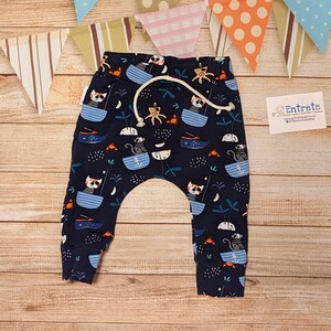May include: Navy blue baby pants with a fun print of cats in boats, anchors, and palm trees. The pants have a drawstring waist and a relaxed fit.