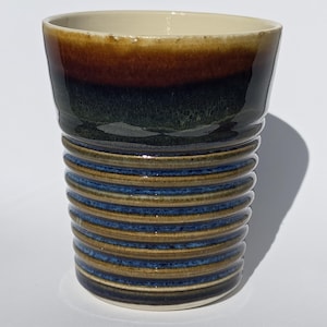 May include: A ceramic cup with a brown, green and blue glaze. The cup has a ribbed design and a white interior.