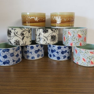 May include: A set of eight ceramic bowls featuring a variety of floral patterns. The bowls are stacked in a pyramid shape, with two brown bowls at the top, followed by three white bowls with black floral designs, and three bowls with blue and white floral designs.