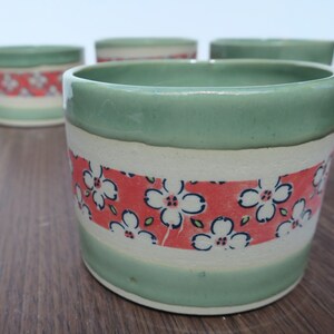 May include: Four green ceramic bowls with a white band and a red band with white floral pattern.