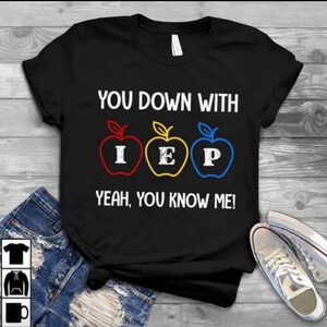 Pode incluir: Camiseta preta com o texto "You down with IEP? Yeah, you know me!" e três maçãs vermelhas, amarelas e azuis com as letras I, E e P nelas.