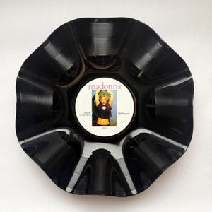May include: A black vinyl record bowl with a scalloped, wavy edge. The center label features the text 'madonna' in purple, with the song titles 'HOLIDAY' and 'THINK OF ME' printed on either side of a photograph of the artist.