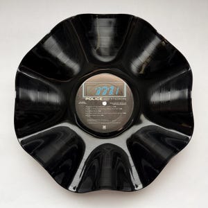 May include: A black vinyl record bowl shaped with eight distinct, curved, and fluted edges. The center label features the text The Police Ghost in the Machine, along with a track list including Spirits in the Material World and Invisible Sun.