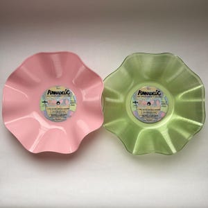 May include: Two bowls shaped like vinyl records with wavy, scalloped edges. One bowl is solid pastel pink, and the other is translucent light green. Each features a central label reading Funkadelic One Nation Under a Groove.