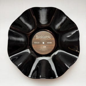 May include: A black vinyl record bowl with a scalloped, wavy edge. The center label features a wood-grain pattern with the text DANGEROUS, The Double Album, and MORGAN WALLEN, along with a tracklist for Side 1 printed in white text.