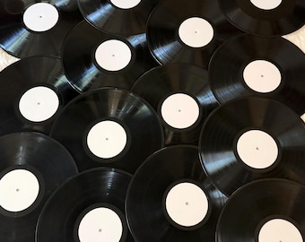 May include: A collection of multiple black vinyl records arranged in an overlapping pattern. Each circular record features a smooth, glossy black surface with a plain, solid white circular label in the center, showing no text or graphics.