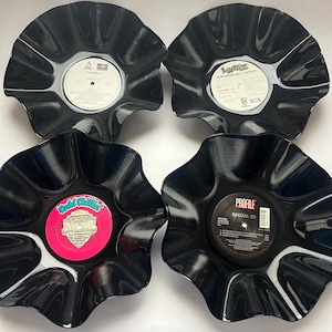 Könnte beinhalten: Vier Schalen aus wiederverwendeten schwarzen Schallplatten mit gewellten, gebogten Rändern. Jede Schale hat ein zentrales Plattenlabel: ein weißes Canibus-Label, ein weißes LUNIZ-Label, ein pinkes Cold Chillin'-Label und ein schwarzes Profile Special Ed-Label.
