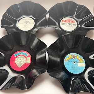 May include: Four black vinyl record bowls with wavy, flared edges. The center labels feature text including Clipse Lord Willin, The Game How We Do, Big Daddy Kane, and Full City Modern Urban Music. Each bowl is made from a repurposed record.