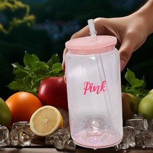 May include: A clear plastic tumbler with a pink lid and straw. The tumbler has the word "Pink" written on it in pink lettering. The tumbler is sitting on a wooden surface with ice cubes and fruit.