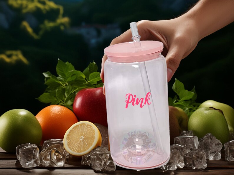 May include: A clear plastic tumbler with a pink lid and straw. The tumbler has the word "Pink" written on it in pink lettering. The tumbler is sitting on a wooden surface with ice cubes and fruit.