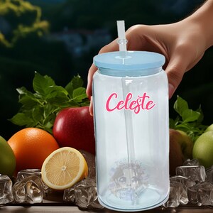 May include: A clear plastic tumbler with a blue lid and a straw. The tumbler has the name "Celeste" written on it in pink letters. The tumbler is surrounded by fruit and ice cubes.