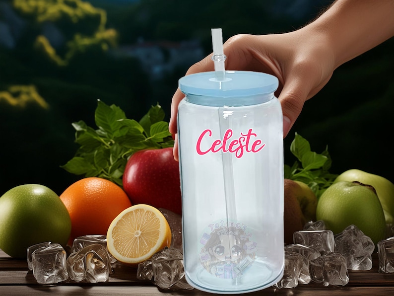 May include: A clear plastic tumbler with a blue lid and a straw. The tumbler has the name "Celeste" written on it in pink letters. The tumbler is surrounded by fruit and ice cubes.