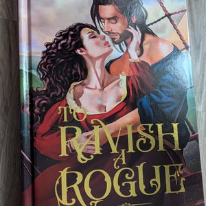 May include: A book cover featuring a romantic scene with a man and woman. The title "To Ravish a Rogue" is in gold lettering. The author's name, C.M. Nascosta, is also in gold. The cover is for a "Talons & Temptations Historical Monster Romance".
