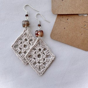 May include: A pair of crocheted square earrings with brown glass beads. The earrings are on a white background.