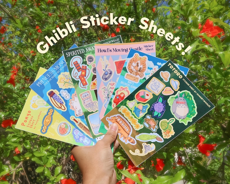 May include: A hand displays a collection of Ghibli-themed sticker sheets. The sheets showcase characters and scenes from films like "Spirited Away," "Howl's Moving Castle," "Princess Mononoke," "Ponyo," and "Totoro." The words "Ghibli Sticker Sheets!" are written at the top.