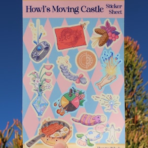 May include: A sticker sheet with illustrations from "Howl's Moving Castle." The sheet has a pink and blue diamond pattern background. Stickers include a ring, a red banner, a braid, a hand with light, a vase of flowers, a pan with food, and a cow.