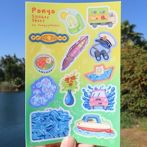May include: A sticker sheet featuring cartoon illustrations of a pink car, a boat, a truck, and a squid. The sheet is labelled "Ponyo Sticker Sheet by HungryWhales". The background is a gradient of green and yellow, with a hand holding the sheet.