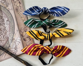 May include: Four fabric hair ties in the colors of the Hogwarts houses: blue and gray, green and silver, yellow and black, and red and gold. The hair ties are tied in a bow shape.