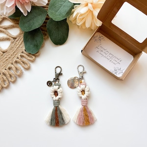 May include: Two handmade macrame keychains with a white and brown tassel and a white and pink tassel. Each keychain has a small silver charm with the text "You are my sunshine, you make me happy" on it. The keychains are displayed in a small brown box with a clear window. The box has a white card inside with the text "I loved you every second of your life and will love you for every second of mine."