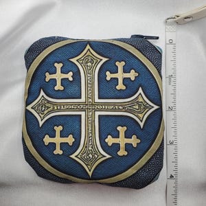 May include: A square, zippered coin purse with a blue background and a gold and cream-colored cross design. The purse is approximately 4 inches wide. The zipper is black, and the purse has a cream-colored strap.