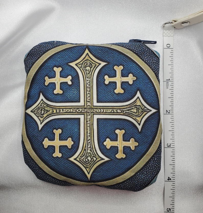 May include: A square, zippered coin purse with a blue background and a gold and cream-colored cross design. The purse is approximately 4 inches wide. The zipper is black, and the purse has a cream-colored strap.
