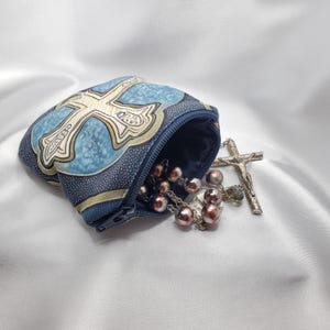 May include: A rosary with brown beads and a silver crucifix spills from a blue pouch with a cross design. The pouch has a zipper closure and is made of patterned fabric.