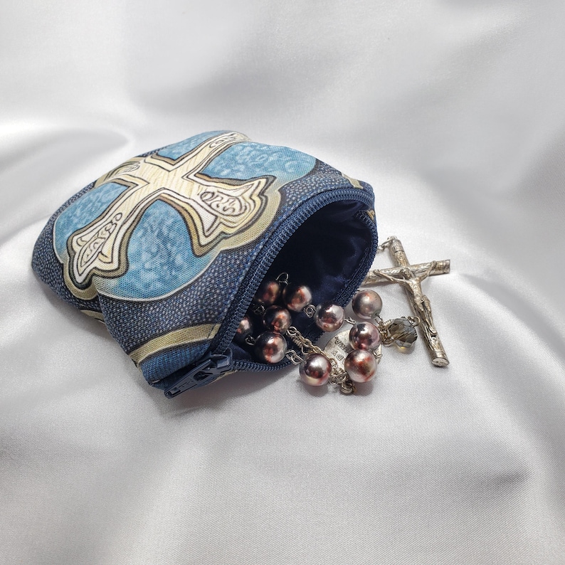 May include: A rosary with brown beads and a silver crucifix spills from a blue pouch with a cross design. The pouch has a zipper closure and is made of patterned fabric.