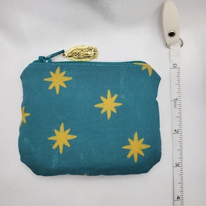 May include: Teal coin purse with a gold star pattern and a gold zipper pull. The purse is approximately 4 inches wide. A white measuring tape is next to the purse.