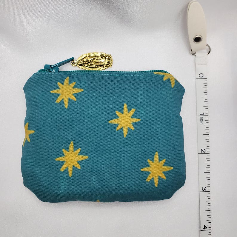 May include: Teal coin purse with a gold star pattern and a gold zipper pull. The purse is approximately 4 inches wide. A white measuring tape is next to the purse.