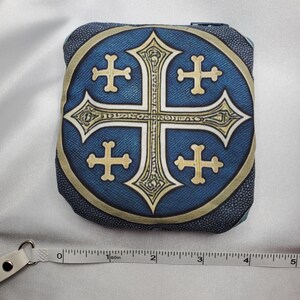 May include: Square, blue fabric pouch with a gold and white cross design. The cross is centered on a blue circle with a gold border. The pouch is approximately 4 inches wide.