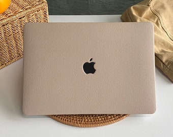 May include: A light beige laptop computer with a black Apple logo on the lid. The laptop is sitting on a woven wicker coaster.