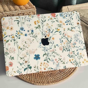 May include: A white laptop skin with a floral pattern featuring small blue, pink, and yellow flowers. The skin has a matte finish and is designed to protect the laptop from scratches and wear.