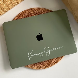 以下が含まれることがあります： 黒いアップルのロゴと蓋に白で「Kanny Garcia」と書かれた緑色のラップトップ