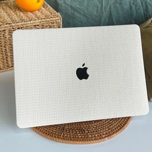 May include: White laptop computer with a woven texture and the Apple logo on the lid. The laptop is sitting on a woven coaster.