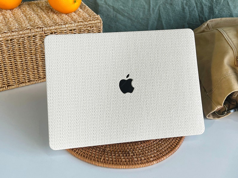 May include: White laptop computer with a woven texture and the Apple logo on the lid. The laptop is sitting on a woven coaster.