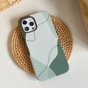 以下が含まれることがあります： 抽象的なデザインの緑と白の携帯電話ケース。ケースにはカメラの切り抜きと黒いアウトラインがあります。