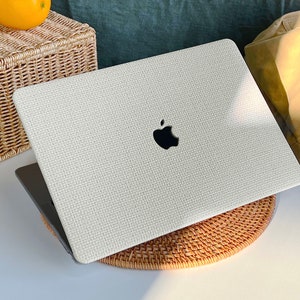 May include: A white laptop with a textured surface and an Apple logo on the lid. The laptop is sitting on a woven mat.