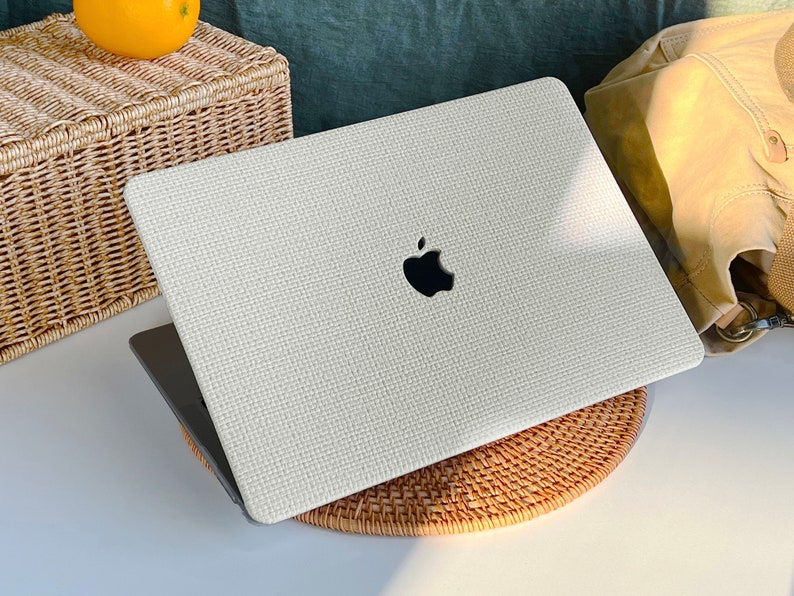 May include: A white laptop with a textured surface and an Apple logo on the lid. The laptop is sitting on a woven mat.