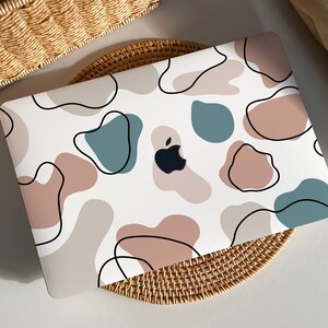 Könnte beinhalten: Ein weißer Laptop mit einem farbenfrohen abstrakten Design mit braunen, blauen und schwarzen Formen. Das Apple-Logo ist auf dem Laptop sichtbar.