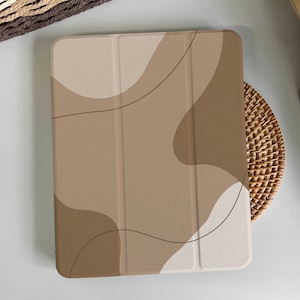 Op de afbeelding: Een beige en bruine tablet hoes met een abstract ontwerp. De hoes heeft een textuur en een subtiel patroon van gebogen lijnen.
