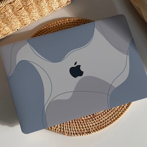 Puede incluir: Un ordenador portátil con un diseño abstracto de color azul claro y gris en la tapa. El logotipo de Apple es visible en la tapa.