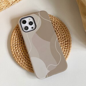 May include: A beige phone case with a white abstract design. The case has a camera cutout and is made of a soft, flexible material.