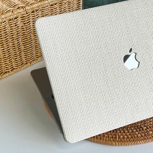 May include: A white laptop computer with a woven texture and an Apple logo on the lid. The laptop is sitting on a woven mat.