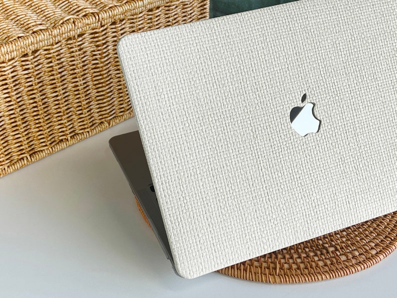May include: A white laptop computer with a woven texture and an Apple logo on the lid. The laptop is sitting on a woven mat.