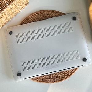 May include: White laptop case with a textured surface and four rubber feet. The case is sitting on a woven mat.