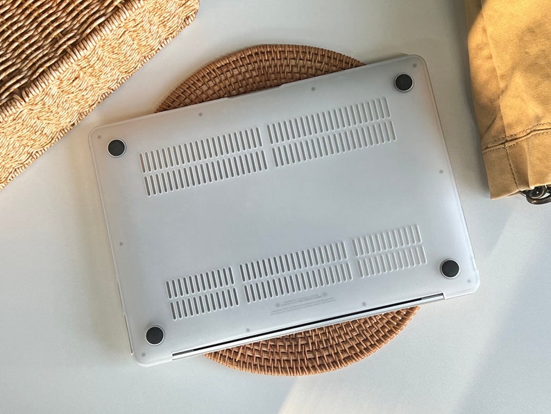 May include: White laptop case with a textured surface and four rubber feet. The case is sitting on a woven mat.