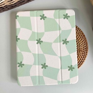 Può includere: Una custodia per iPad a scacchi verdi e bianchi con un motivo ondulato e piccoli disegni di fiori verdi.